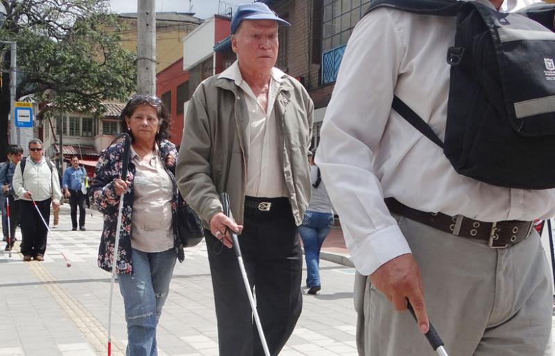 Persona con discapacidad visual caminando por un anden con tabletas podotactiles 