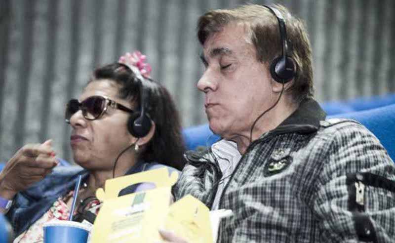 varias pérsonas están en una sala de cine estan comiendo palomitas de maiz y viendo uan película todos usan lentes oscuros y audifonos