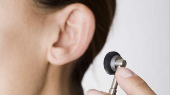 imagen una mano sostiene un auricular en segundo plano se ve la oreja de una mujer joven