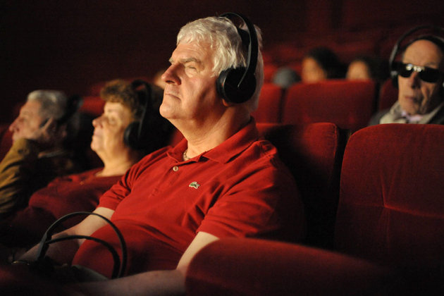 varias personas con discapacidad visual usan audifonos están todos de rojo y están en una sala de cine