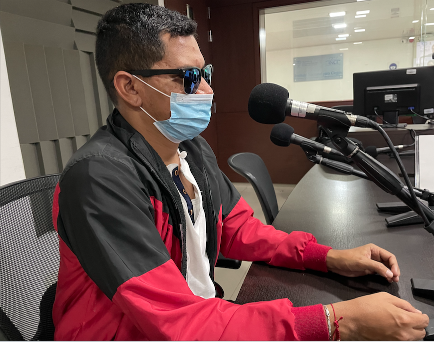 Ronnys lopez en la cabina de INCIRadio, sus manos reposan sobre la mesa, él está frente al micrófono