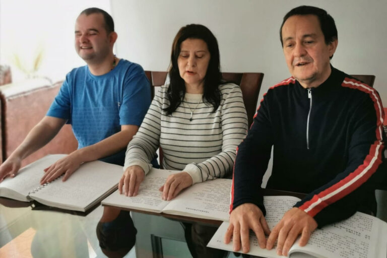tres personas con discapacidad visual leen con sus dedos 