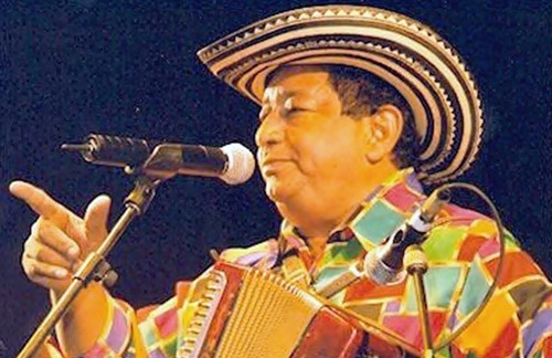 Lisandro viste una camisa multicolor, un sombrero vueltiao, con su mano derecha señala con su dedo indice