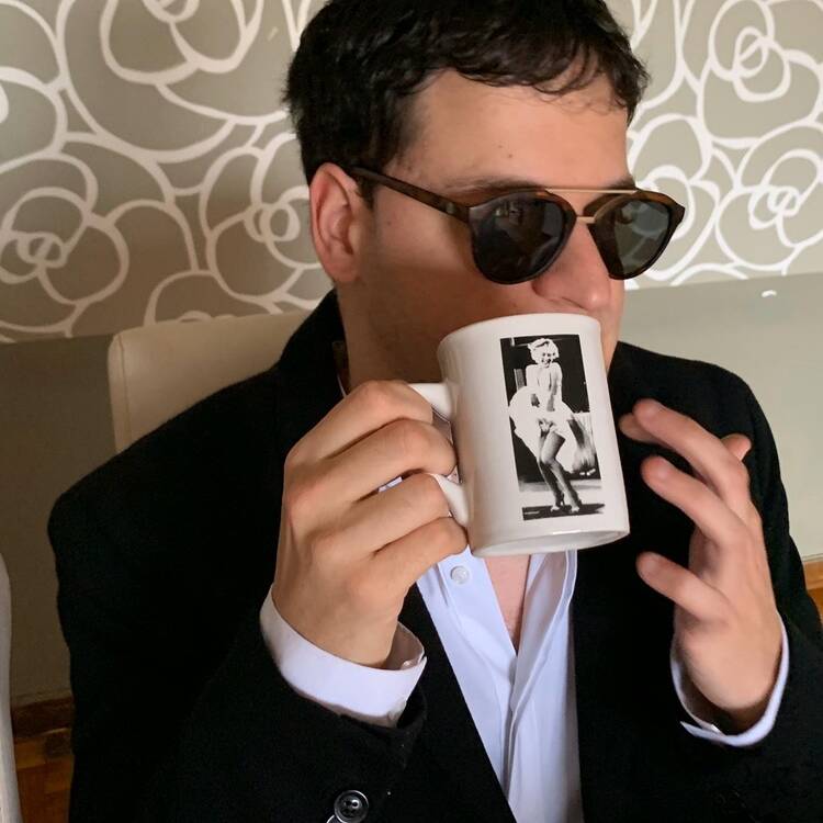 Imagen de Oriol Gómez él sostiene un mug de Marilyn Monroe, él viste un traje oscuro y camisa blanca