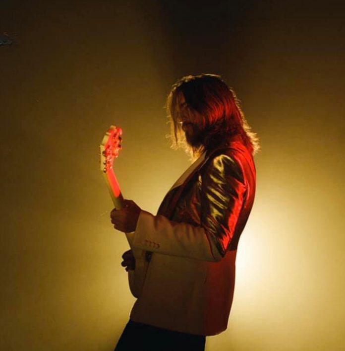 Juanes está de medio lado interpretando con su guitarra la canción dancing in the dark