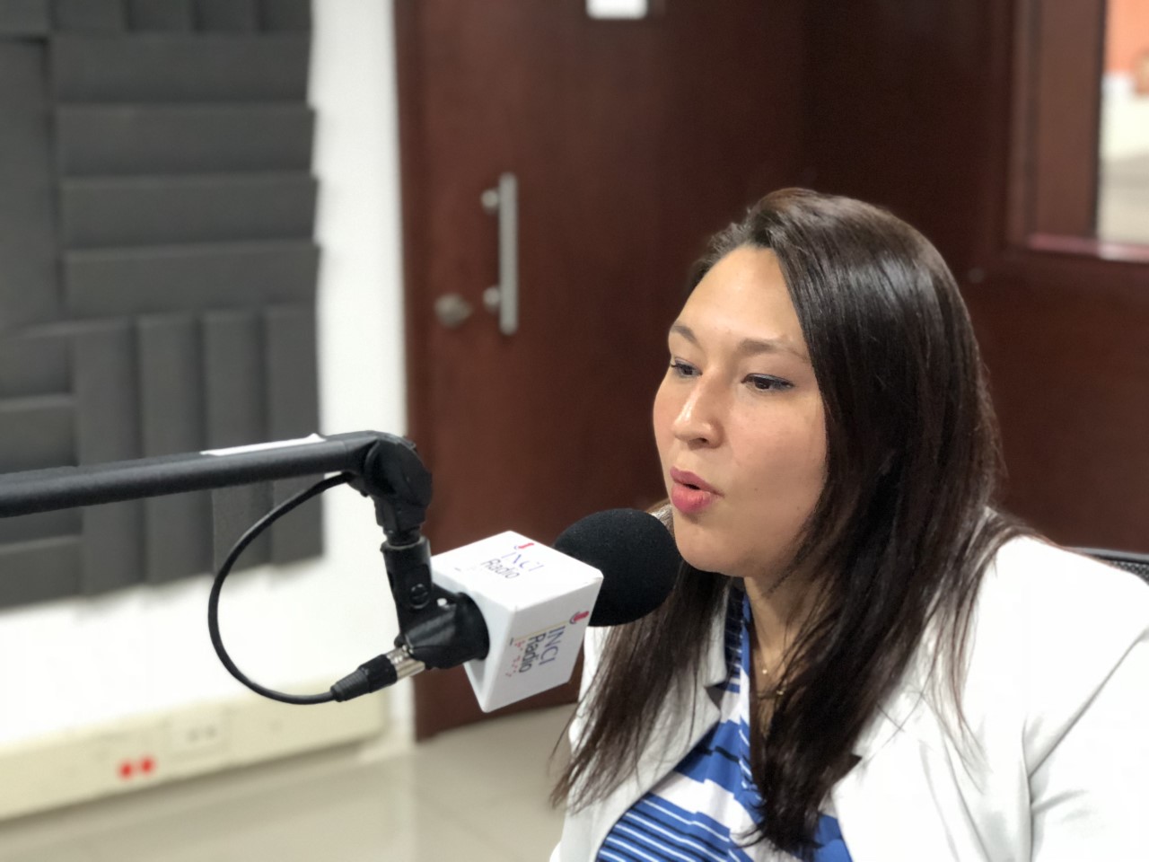 Imagen Leidy HOyos, ella està en la cabina de INCIRadio, viste un blazer de color blanco, frente a ella està el microfono que se logra ver el logo de inciradio, ella se ve seria