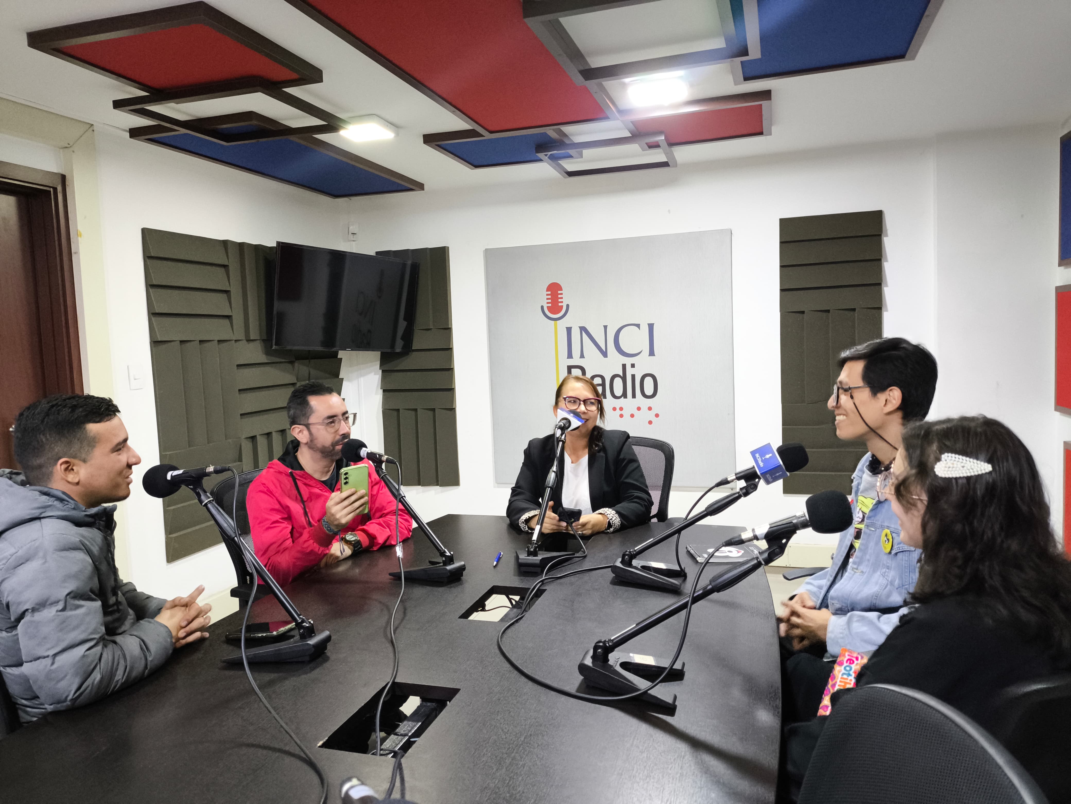 en la mesa de trabajo está el equipo de ciudad al tacto, felipe, juan pablo y myriam a la derecha están los dos invitados, todos sonríen