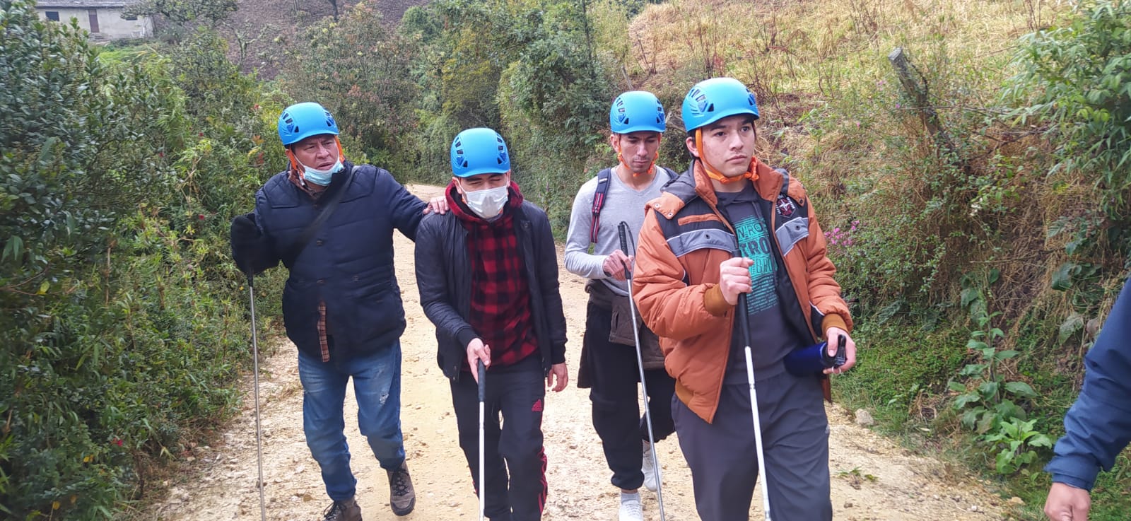 foto haciendo senderismo varias personas con discapacidad visual caminan llevan puestos cascos de protecciòn y van con su bastòn 