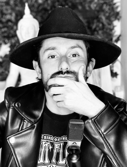 blanco y negro, Henry tiene un sombrero de color negro, chamarra negra de cuero y una camiseta de Pink Floyd, el mira la cámara , se ve un microfóno.