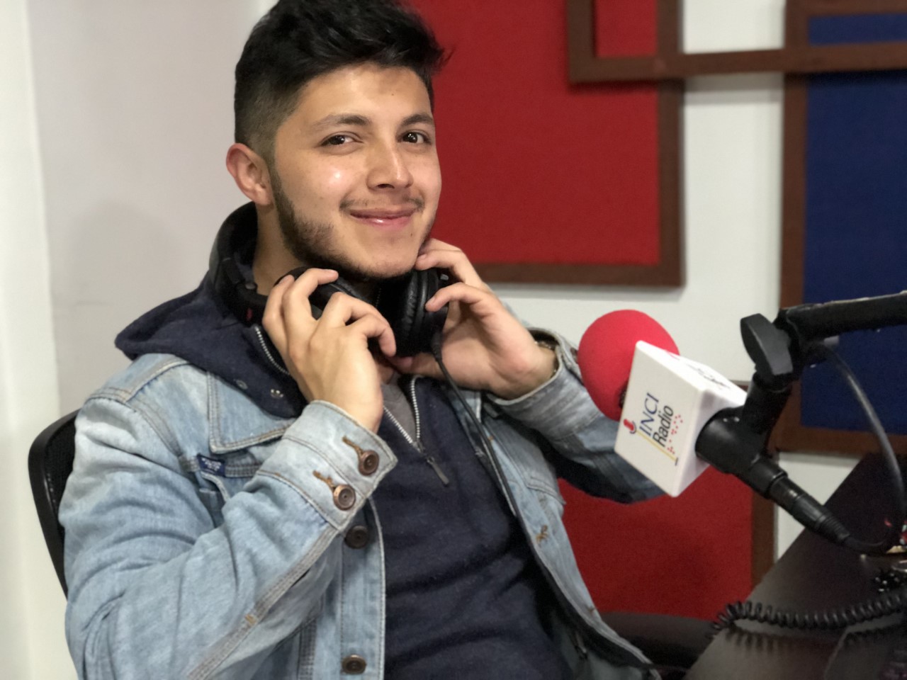 foto de nicolas sanz, él sostiene los audifonos, sonríe frente la micrófono