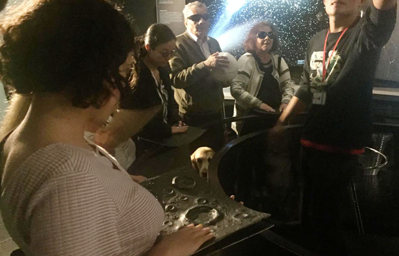 Fotografía, personas con discapacidad visual tocando material didactico del planetario