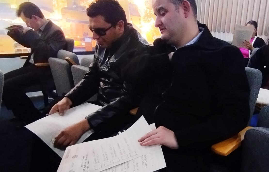 Sergio González junto a otras personas con discapacidad visual analizan tarjetón de votaciones en braille