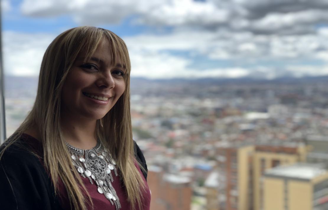 Imagen Adriana en primer plano sonríe, de fondo se ve Bogotá, imagen tomada en el piso 30 del hotel Tequendama