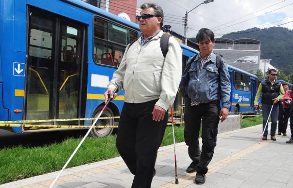 Personas con discapacidad visual caminando por una linea de tabletas podotáctiles