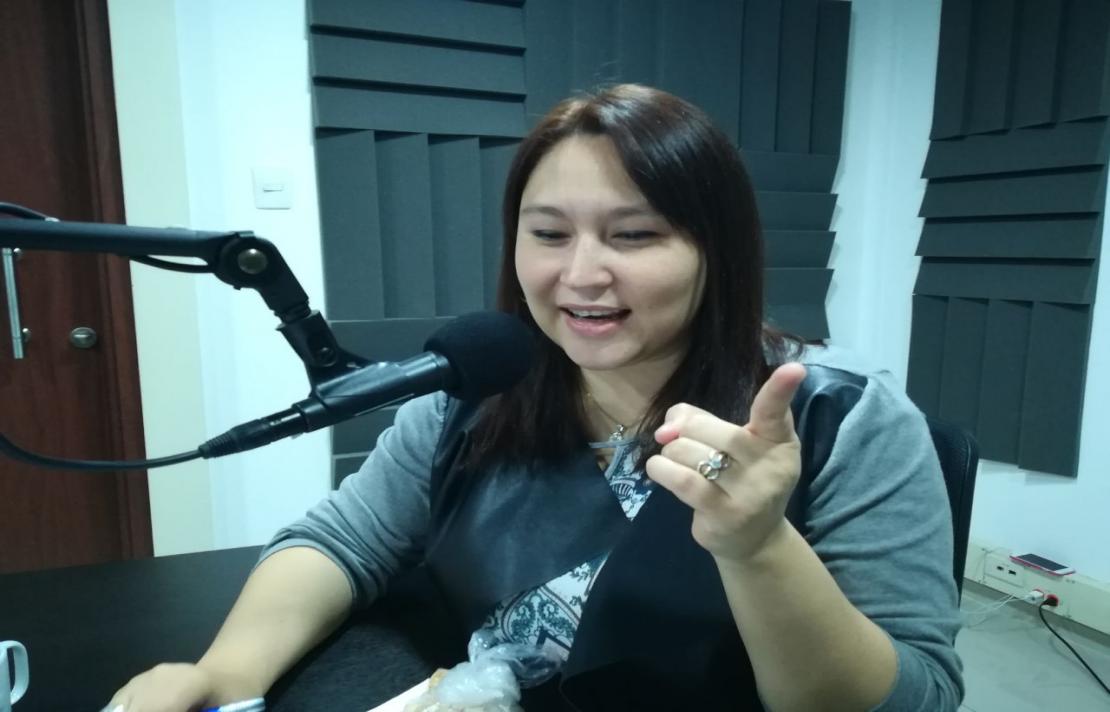 imagen de leidy hoyos en la cabina de inciradio, ella lee un texto, está frente al micrófono con su dedo señala hacia al lado