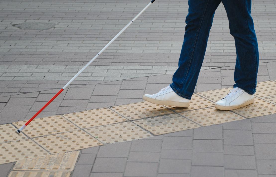 Fotografía - Peatón caminando con bastón sobre baldosas podo táctiles con