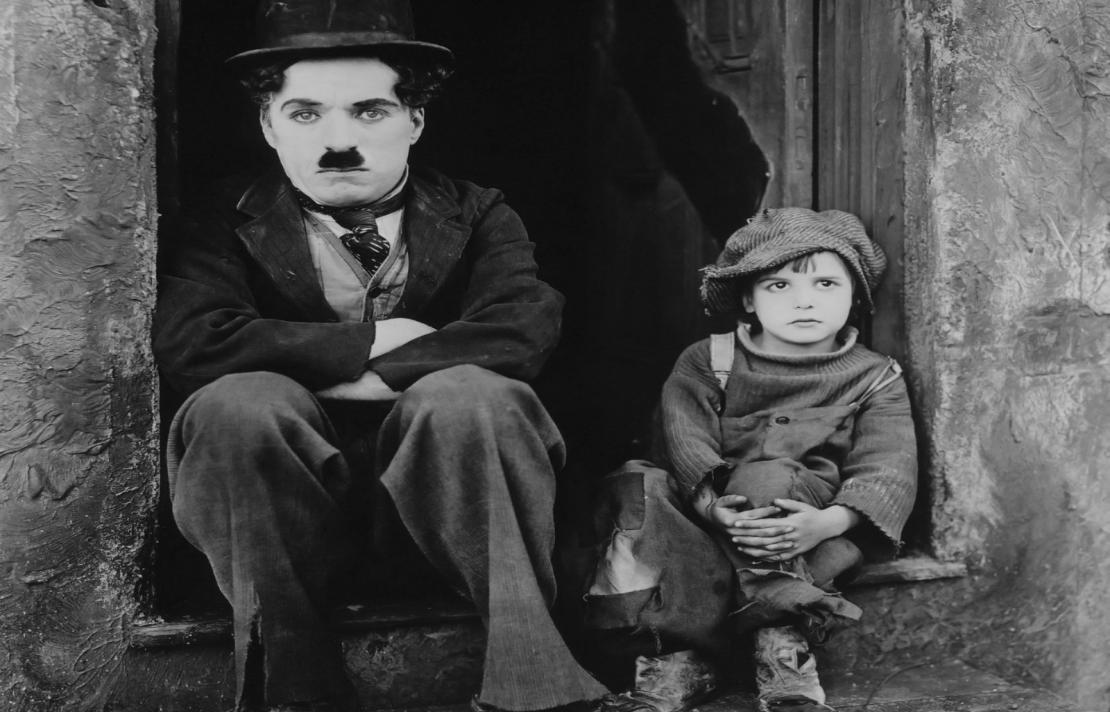 foto de la película de Kid charles Chaplin están sentado junto a Jackie Coogan actor de "The kid", ellos están sentados frente a una puerta