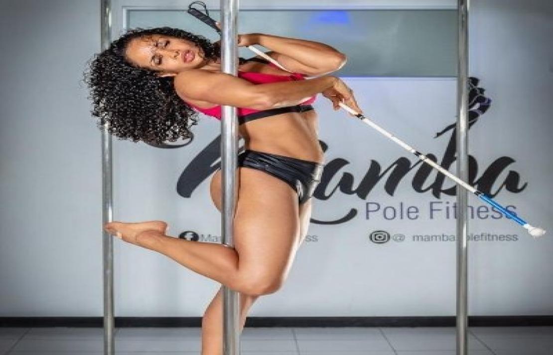 Andrea Herrera practicando pole dance con su mano derecha sostiene su bastón mientras con su pierna derecha se sostiene al pole,