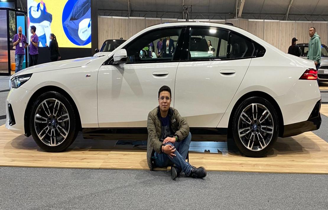 Daniel cortes viste una camisa verde y un jean, está sentado frente a un auto de color blanco