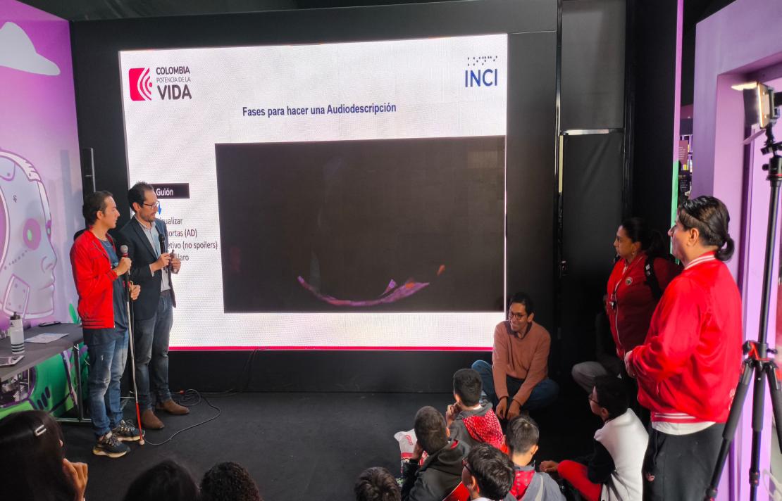 frente a una pantalla gigante están a la izquierda Camilo y Henry a la derecha está Juan Carlos Saenz funcionario del INCI junto a dos docentes,  imágenes del taller