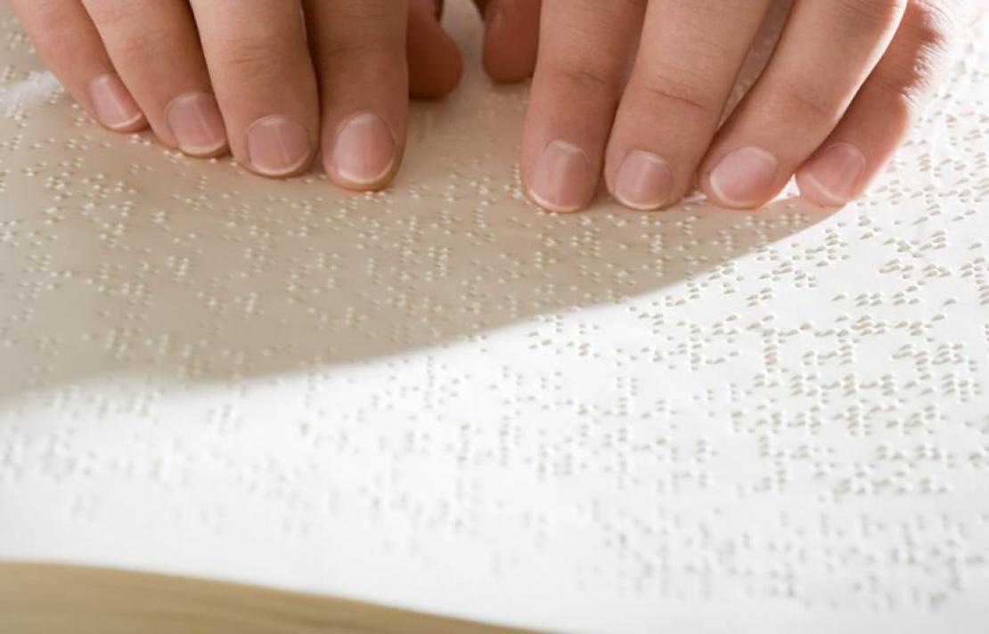 Foto, una cartilla en braille con dos manos pasando sobre los caracteres