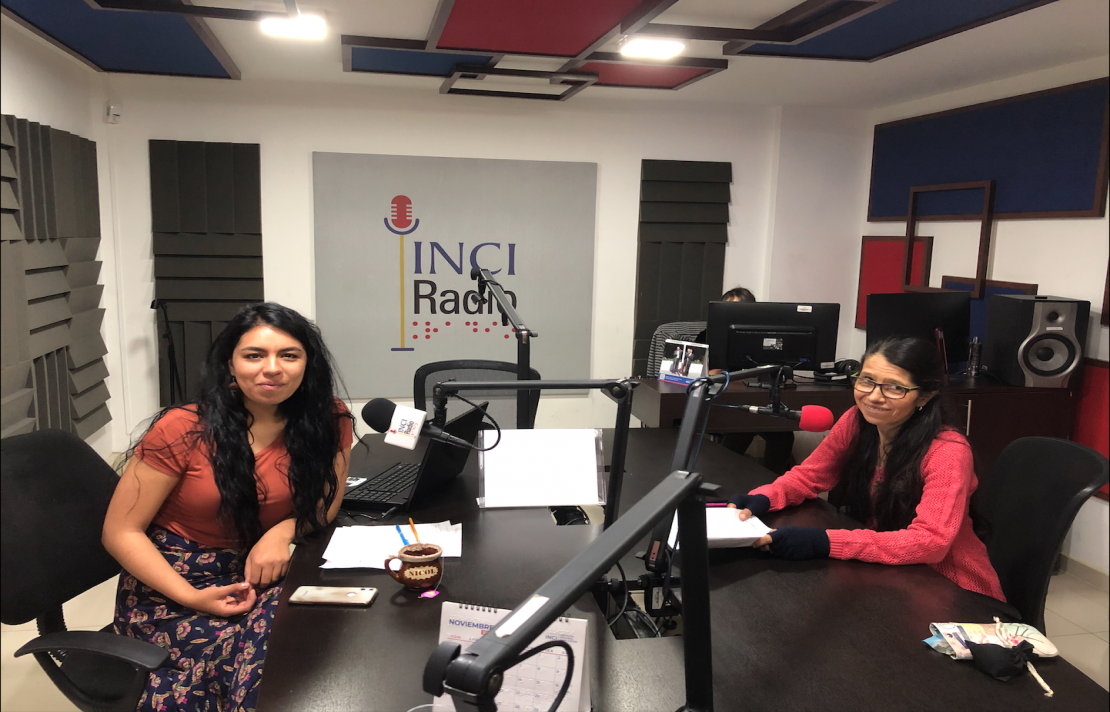 imagen de Nicole Cubillos y Gloria Peña en la cabina de INCIRadio, ellas sonríen frente al micrófono